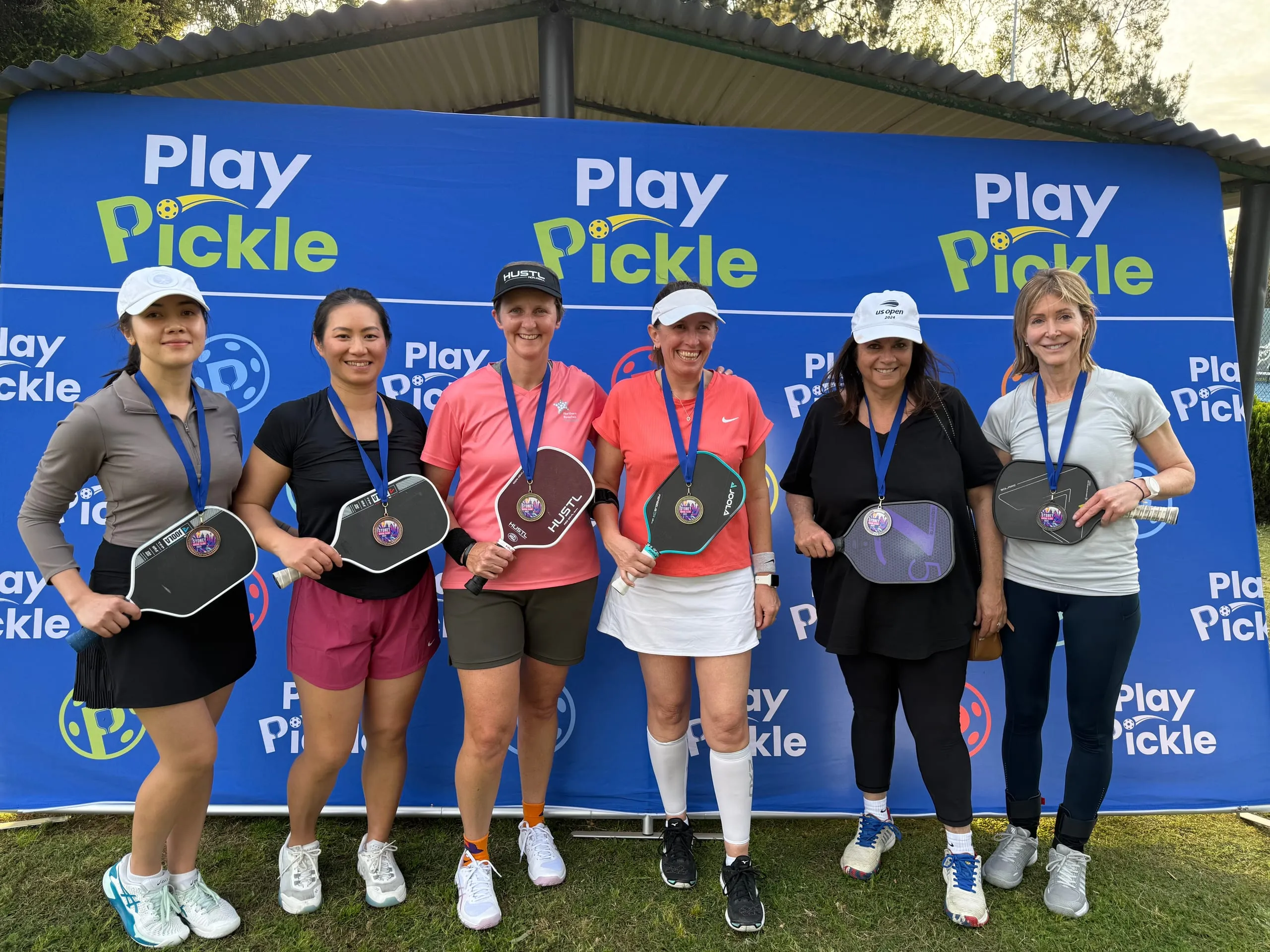A team of six Play Pickle league medallists holding their paddles at the finals