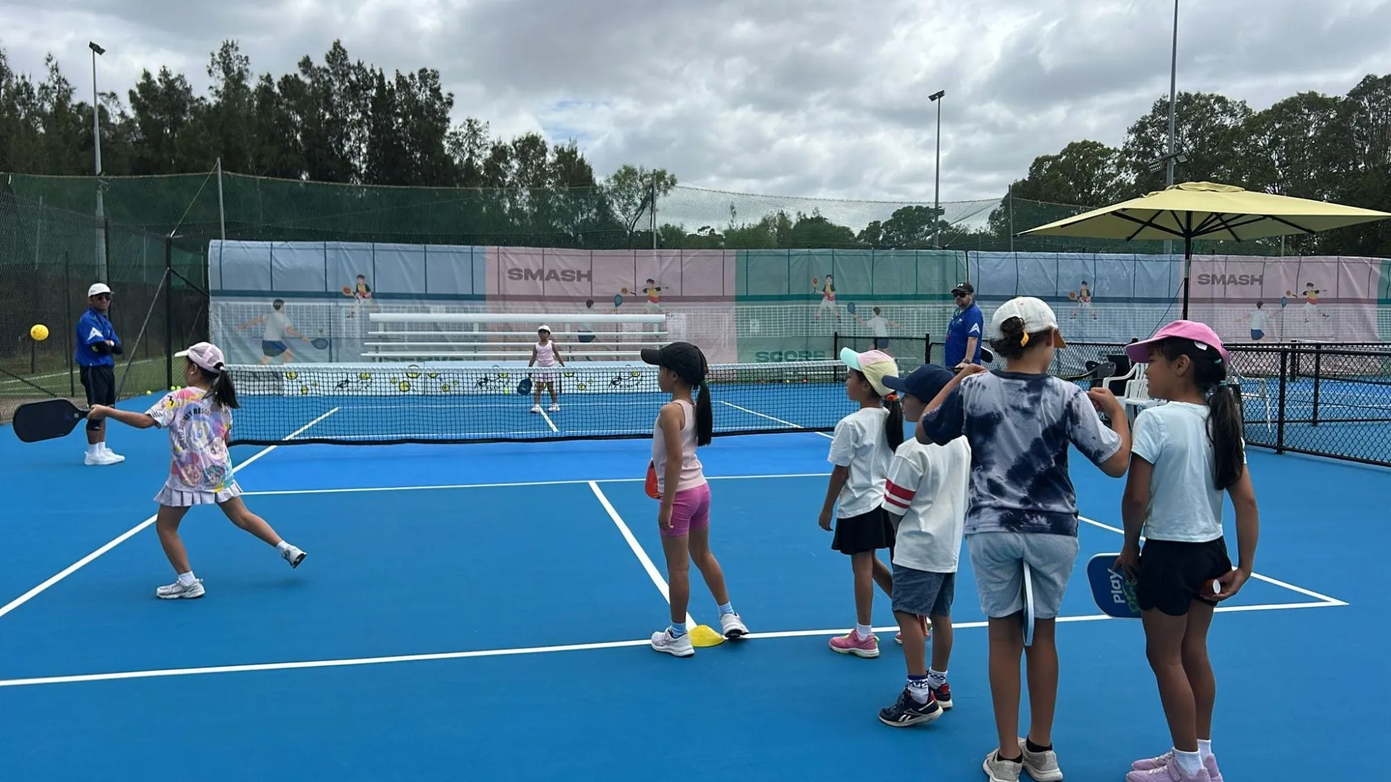 A group of primary-school children lined up for a Play Pickle coaching session on an outdoor court