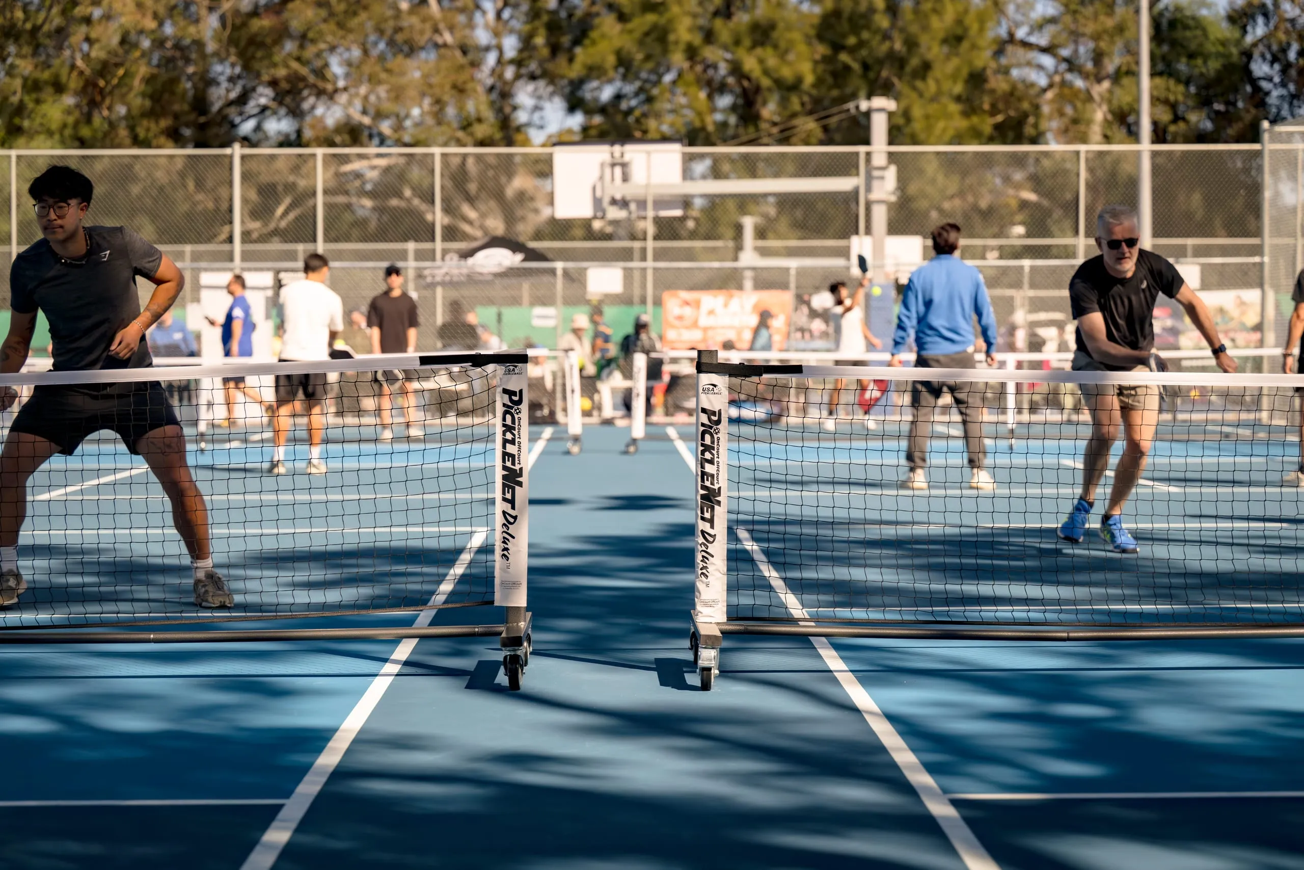 Players competing across several outdoor pickleball courts at a Play Pickle tournament, nets in the foreground
